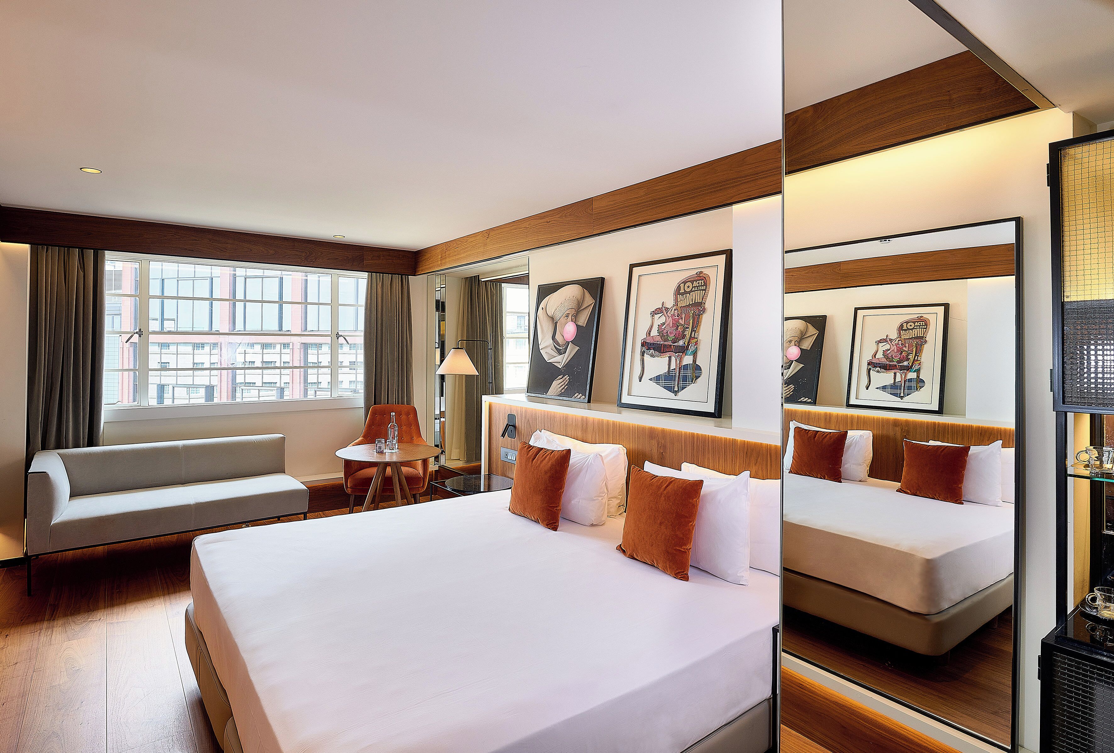 A hotel room with a large bed, a sofa, a small table, and a window with curtains.