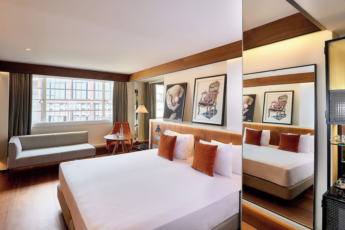 A hotel room with a large bed, a sofa, a small table, and a window with curtains.