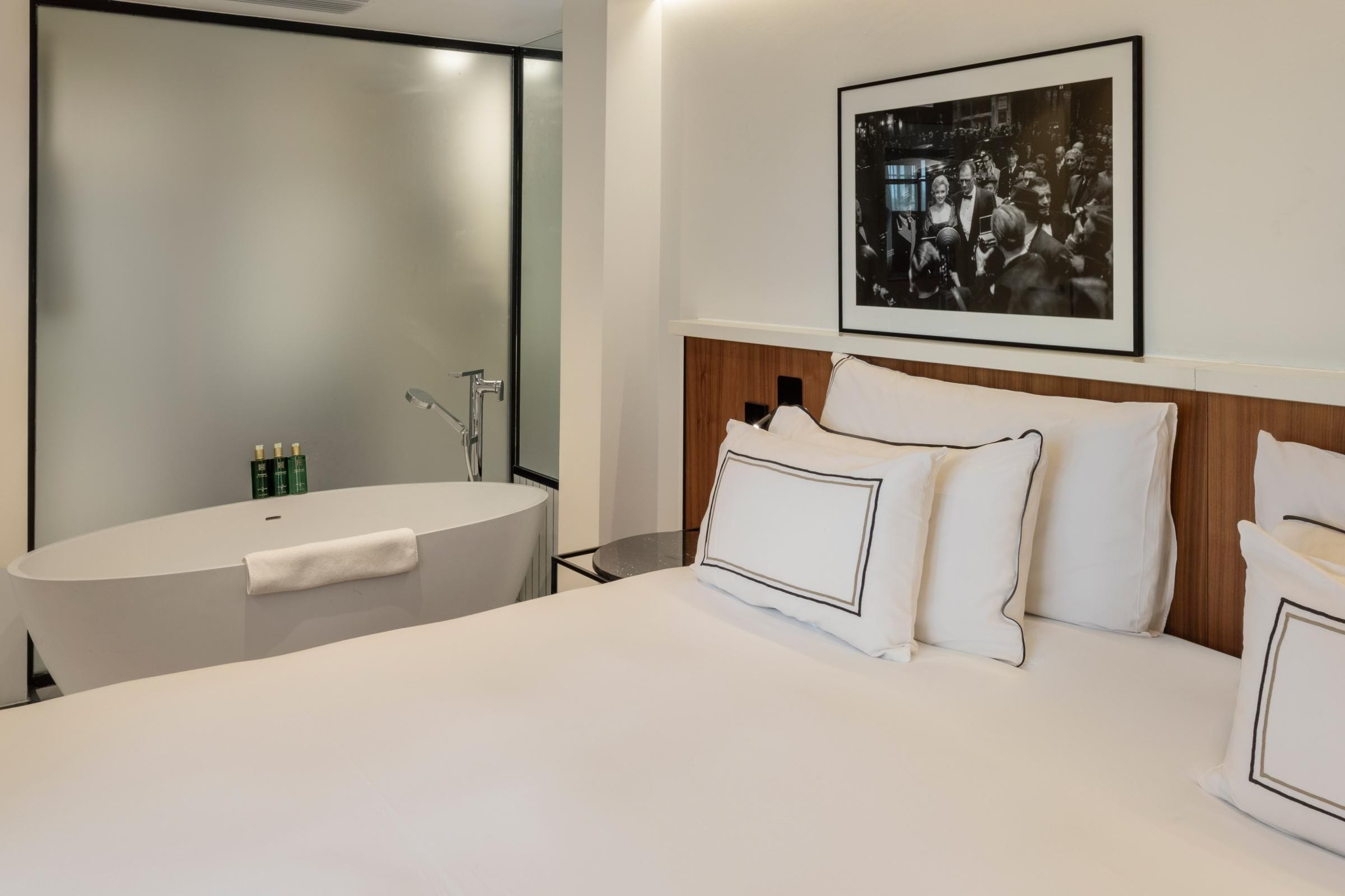 A modern hotel room with a large bed, a wooden headboard, and a framed photograph on the wall.