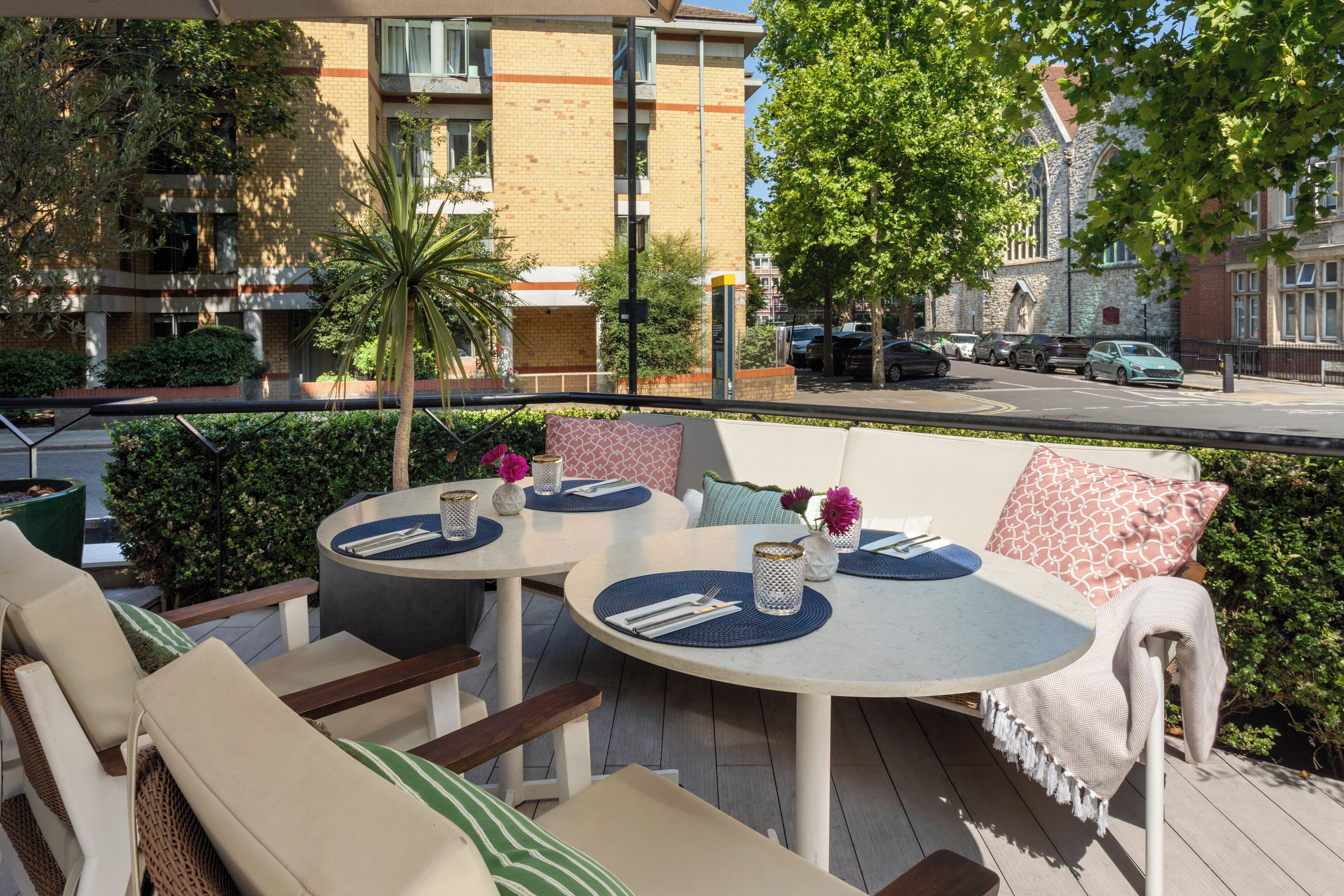 An outdoor seating area with round tables, chairs, and cushions.