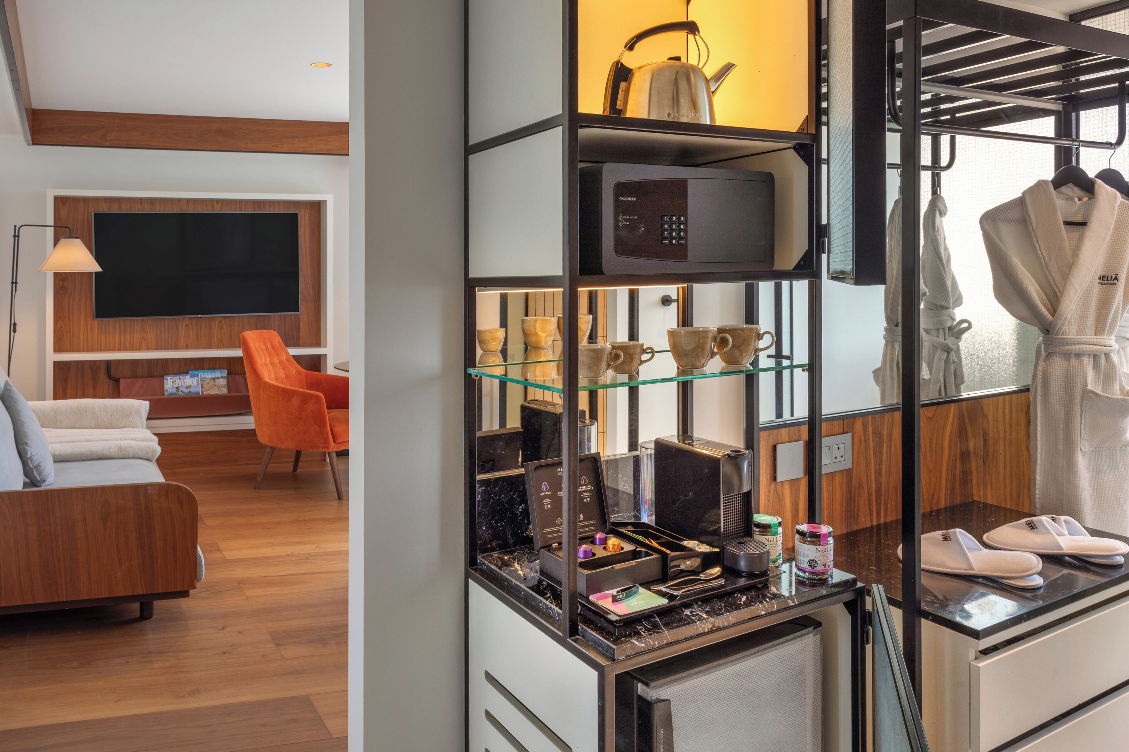 Habitación de hotel con zona de estar, kitchenette y perchero para bata y zapatillas.