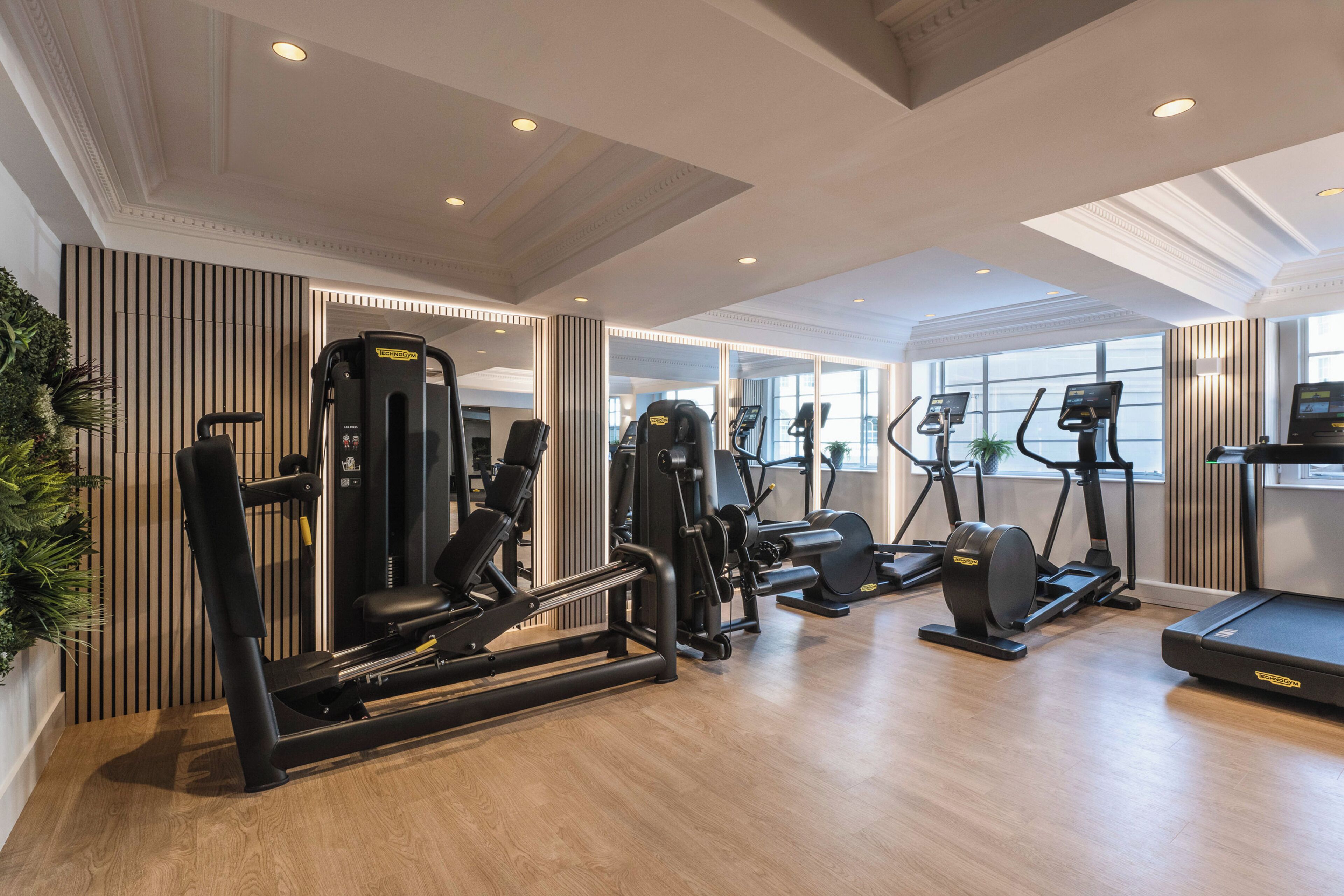 Un gimnasio con equipo de ejercicio diverso, ventanas amplias y suelo de madera.