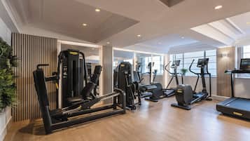 Un gimnasio con equipo de ejercicio diverso, ventanas amplias y suelo de madera.