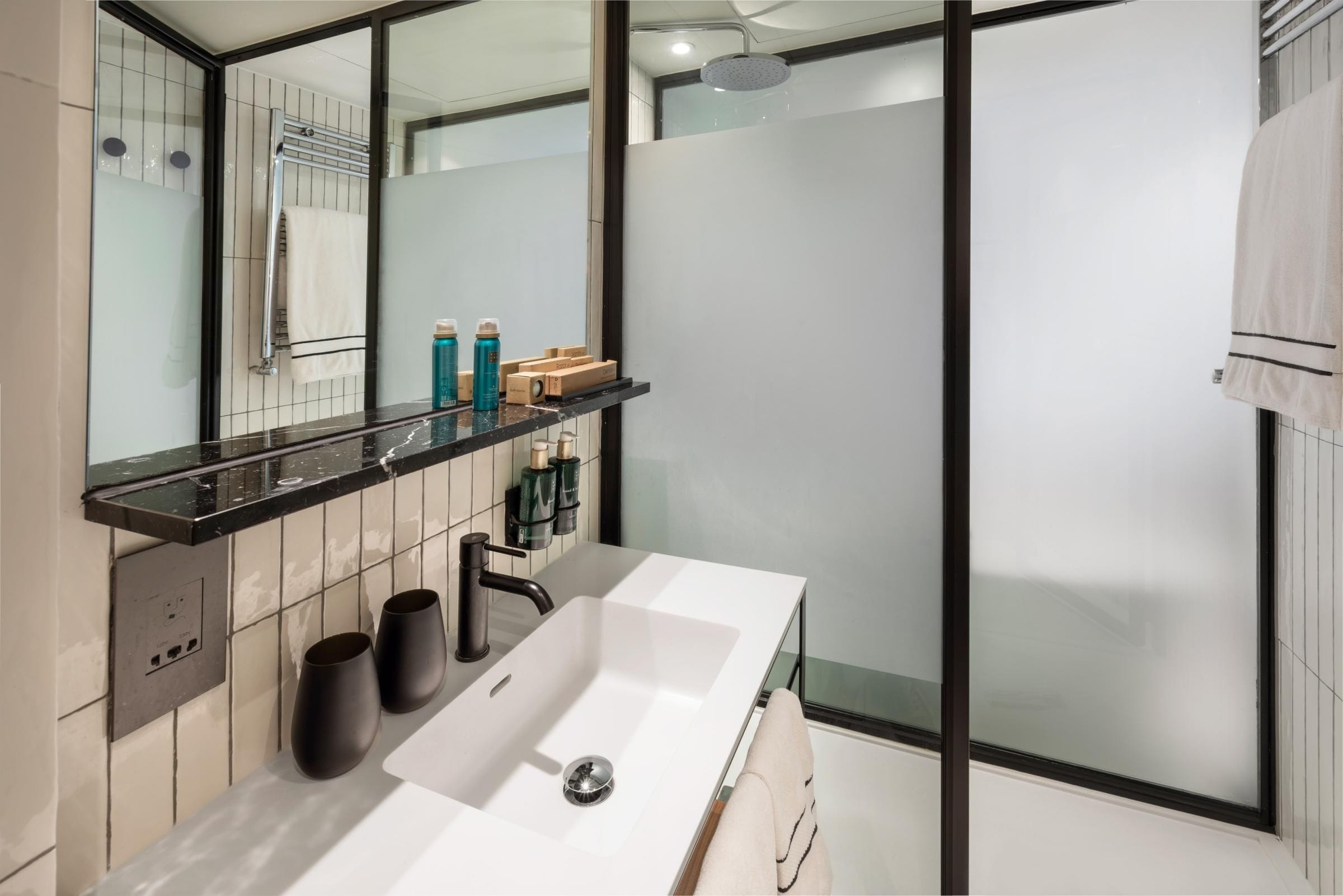 Un baño moderno con un espejo grande, un lavamanos blanco y una cabina de ducha de vidrio.