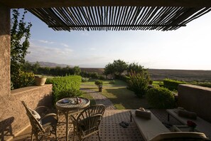 A patio with outdoor furniture, a table, and a view of a landscaped garden and distant mountains. - Le Palais Paysan (Tameslouht)