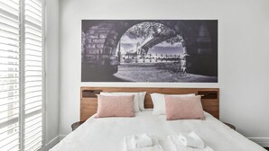 Un dormitorio con una cama grande, ropa de cama blanca y un cuadro de un puente en la pared.