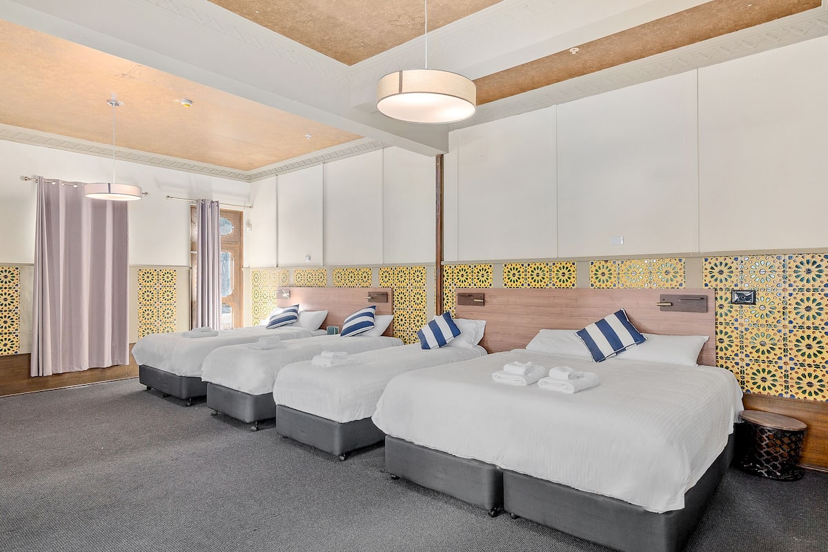 Habitación de hotel con tres camas, un ventanal grande y un papel tapiz decorativo.