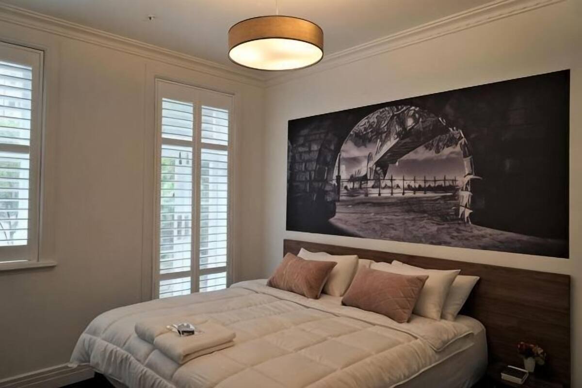 Un dormitorio con una cama grande, un cuadro en la pared y una ventana con persianas.