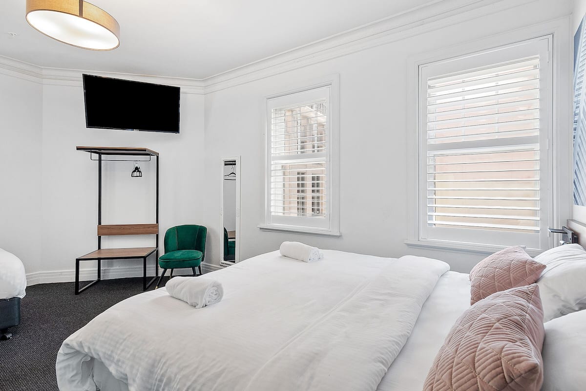 Habitación de hotel con una cama grande, un televisor de pantalla plana en la pared, una silla y una ventana con persianas.