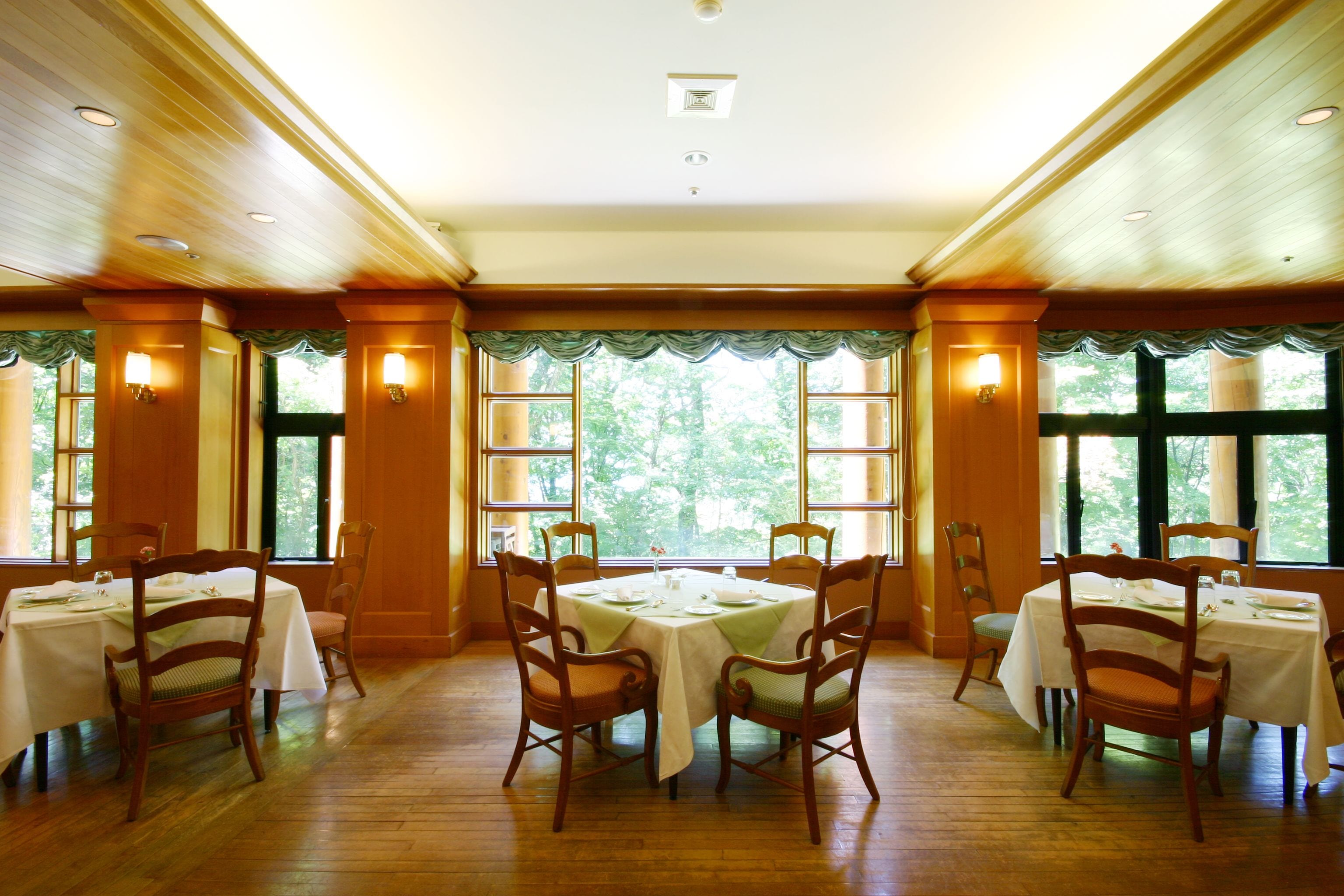 Comedor con paneles de madera, ventanas amplias con cortinas y una mesa central dispuesta para cuatro comensales.