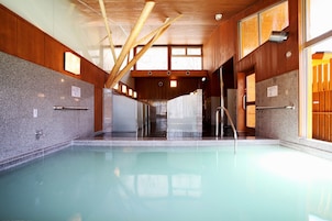 A large indoor swimming pool with wooden beams and a stone wall.