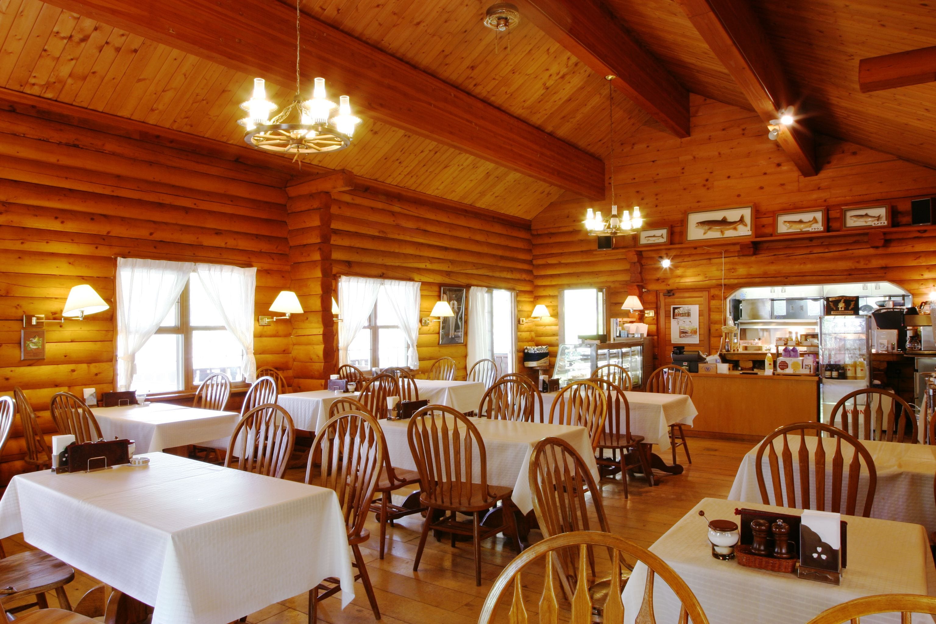 A log cabin-style restaurant with wooden walls and ceilings, multiple tables with white tablecloths, and wooden chairs.