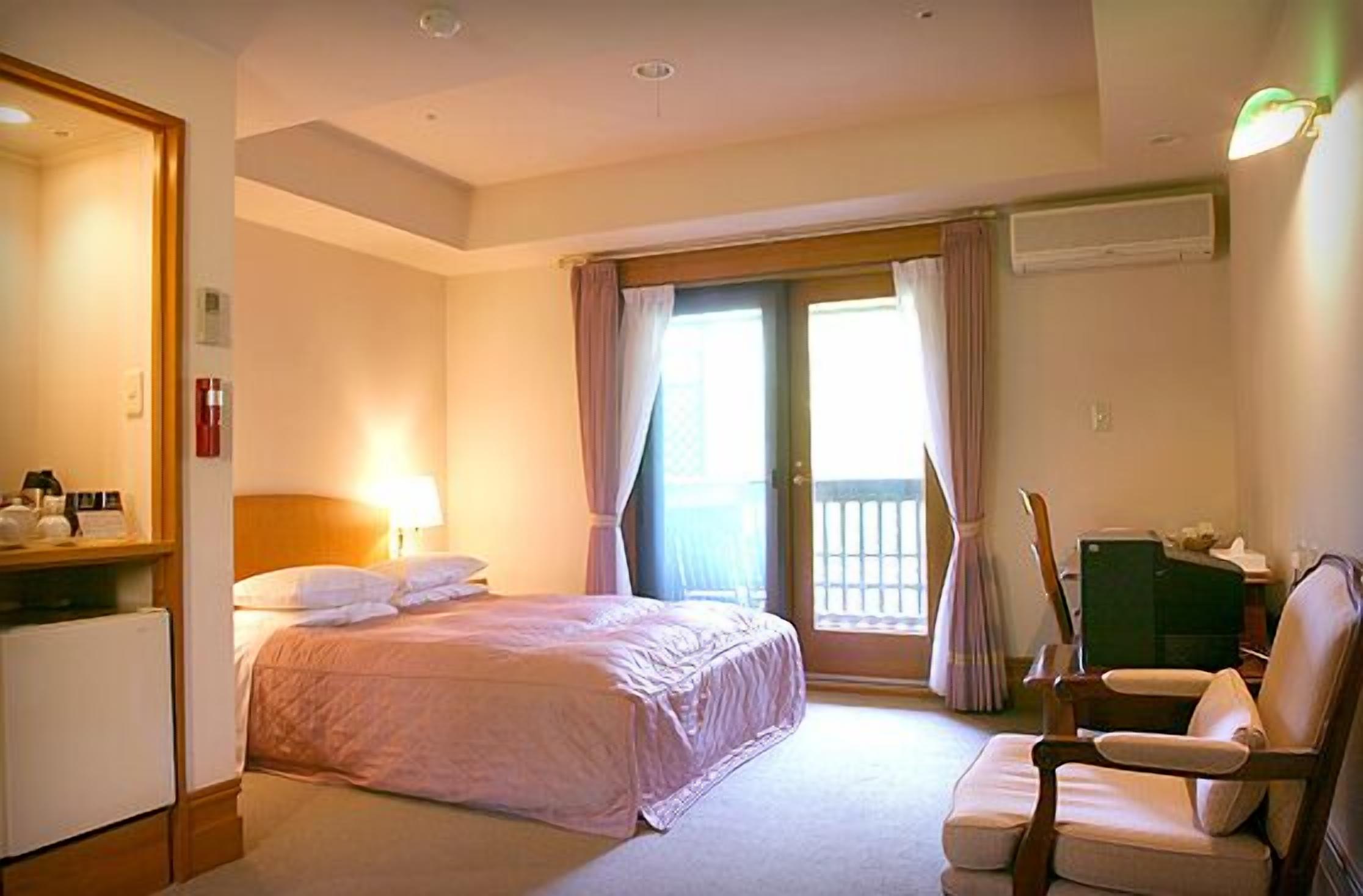 Una camera d'hotel con un letto, una scrivania, una sedia e una finestra con tende.