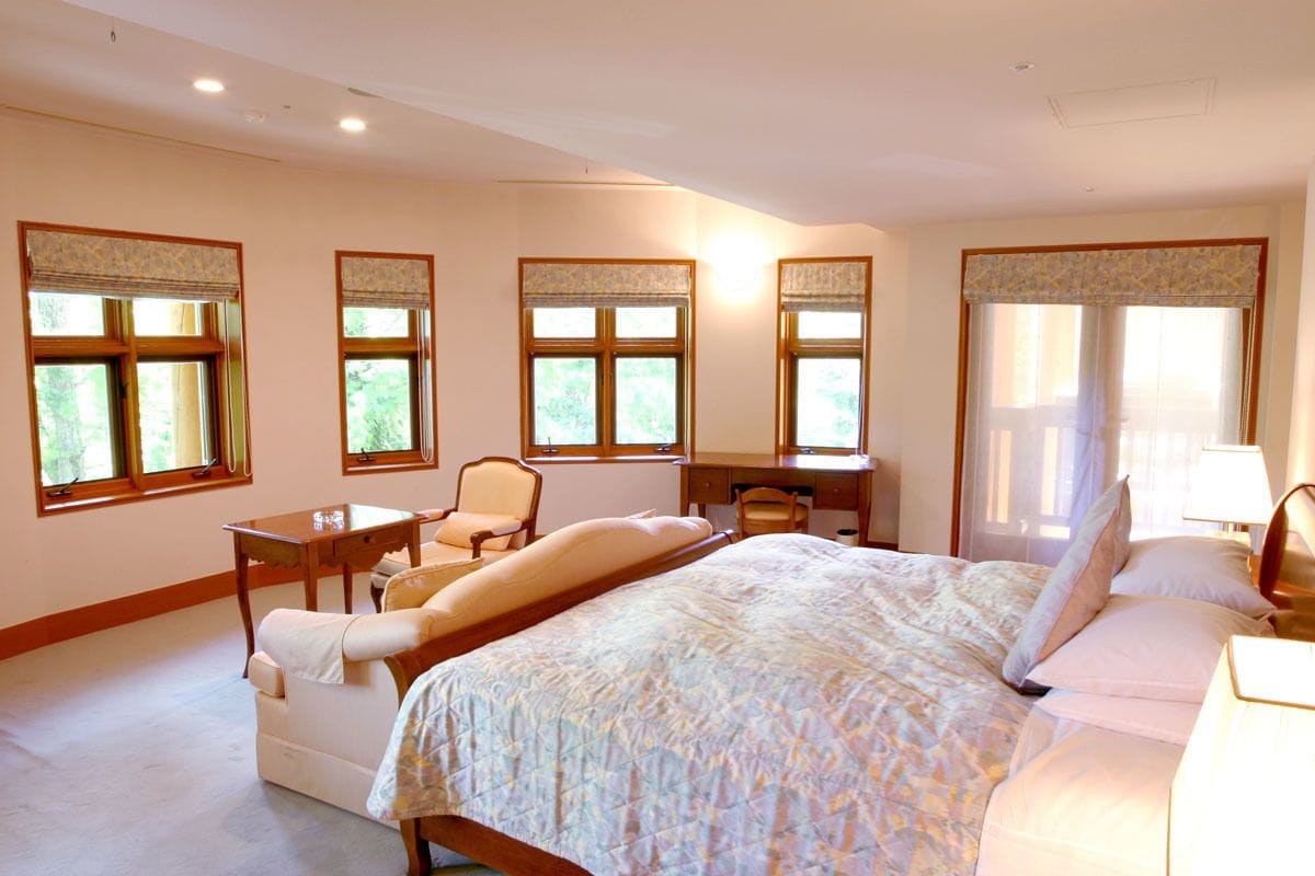 A bedroom with a large bed, two chairs, a desk, and a window with a view of greenery.