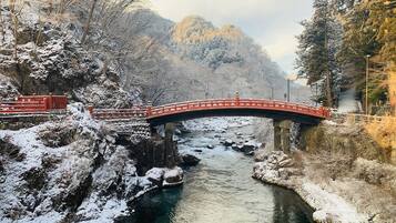 Un puente rojo sobre un río cubierto de nieve, con riberas rocosas y árboles a ambos lados.