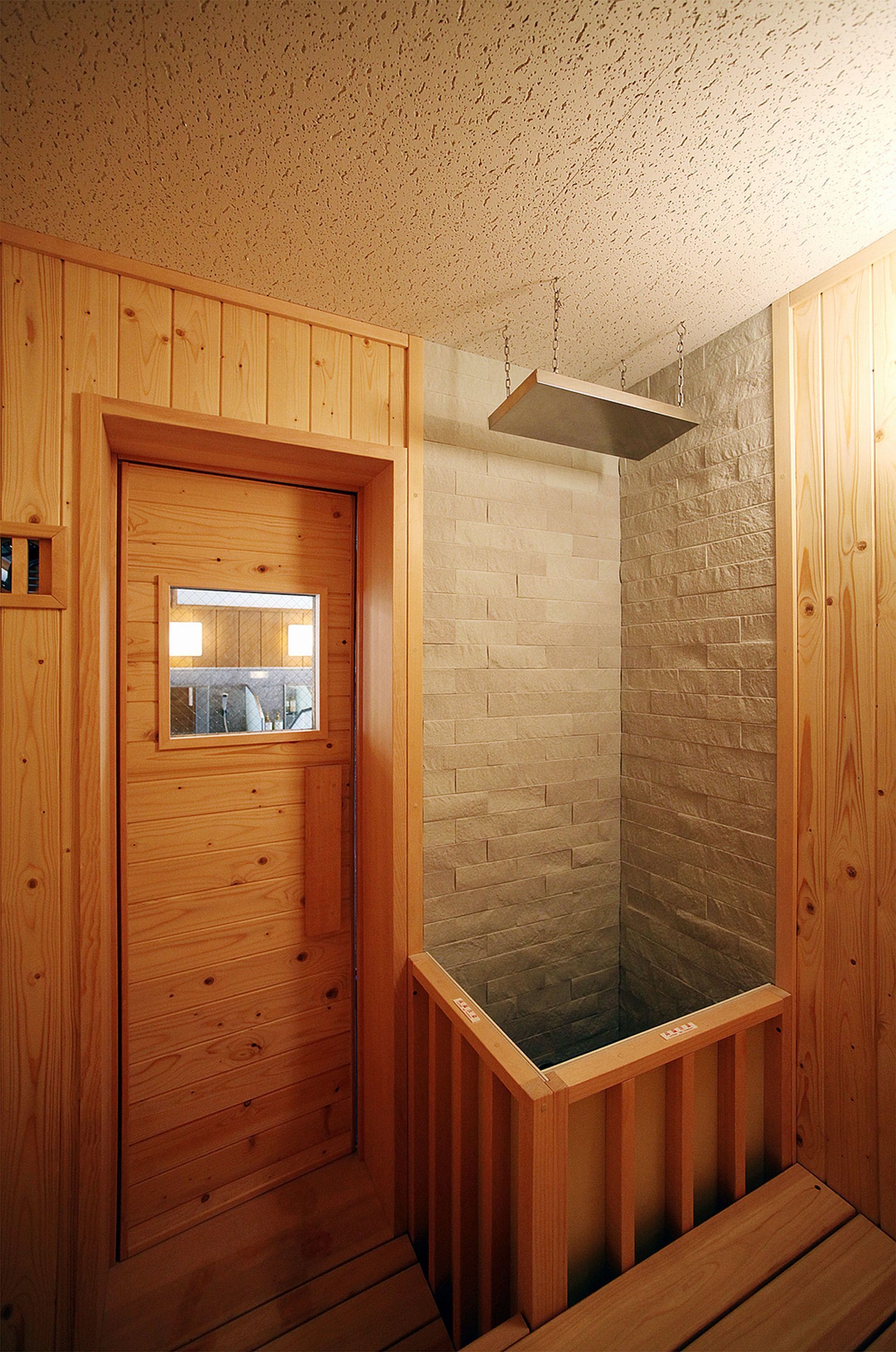 Una sauna de madera con puerta de cristal y pared de piedra.