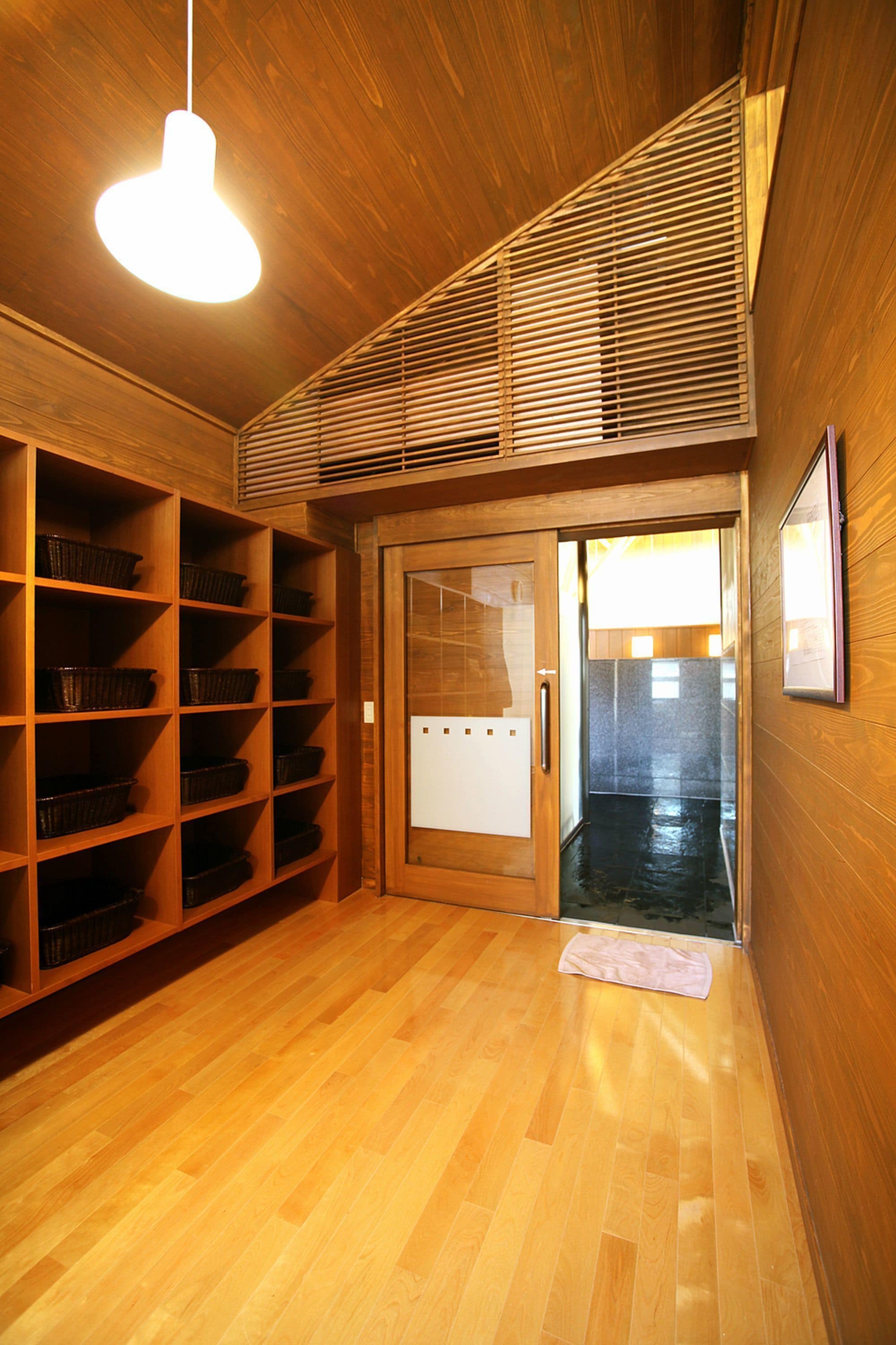 A wooden interior with a sliding door leading to a dark hallway. Shelves line the left wall, and a hanging light fixture is visible.