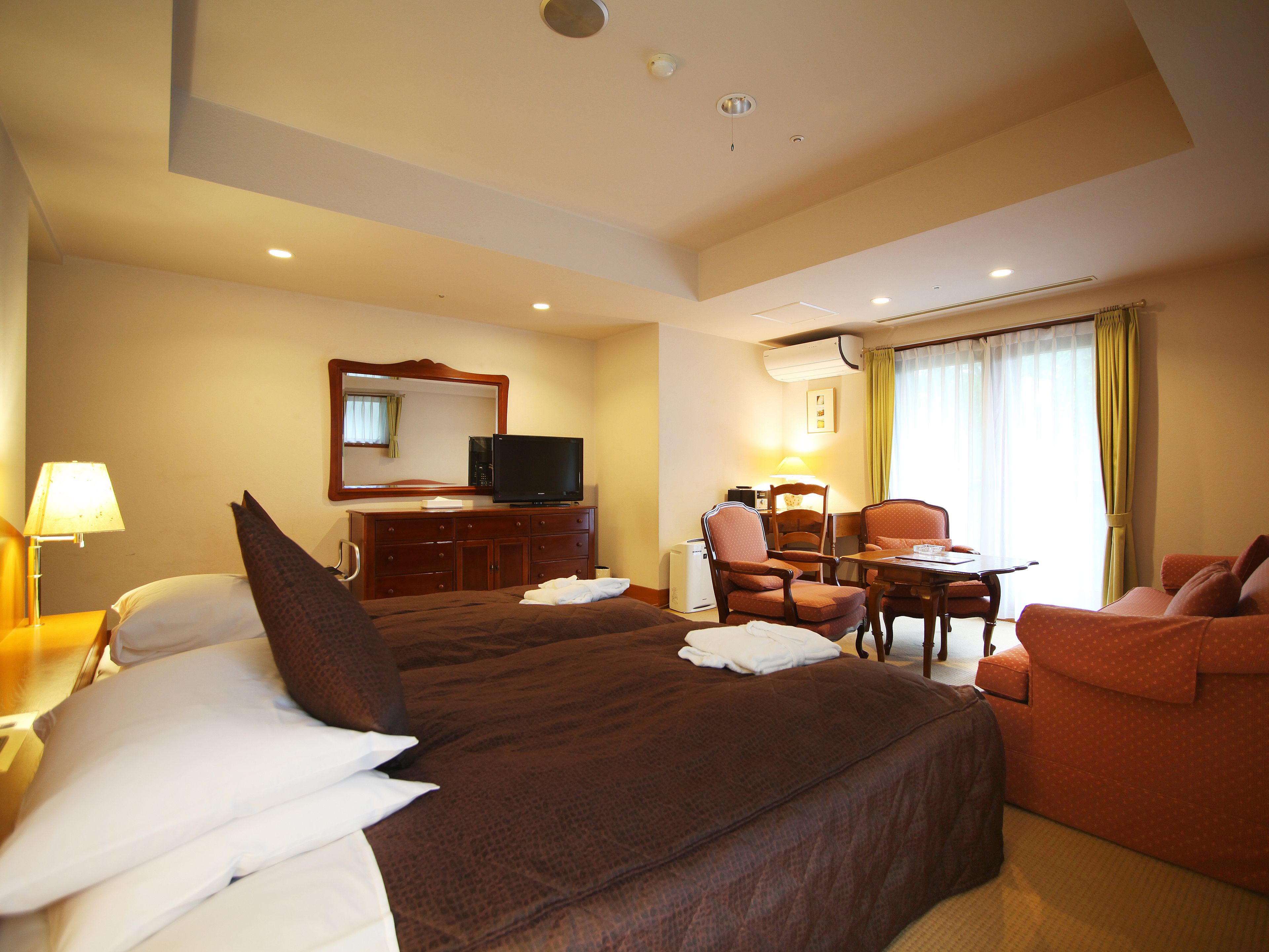 A hotel room with a large bed, a television, a desk with a chair, and a sofa.