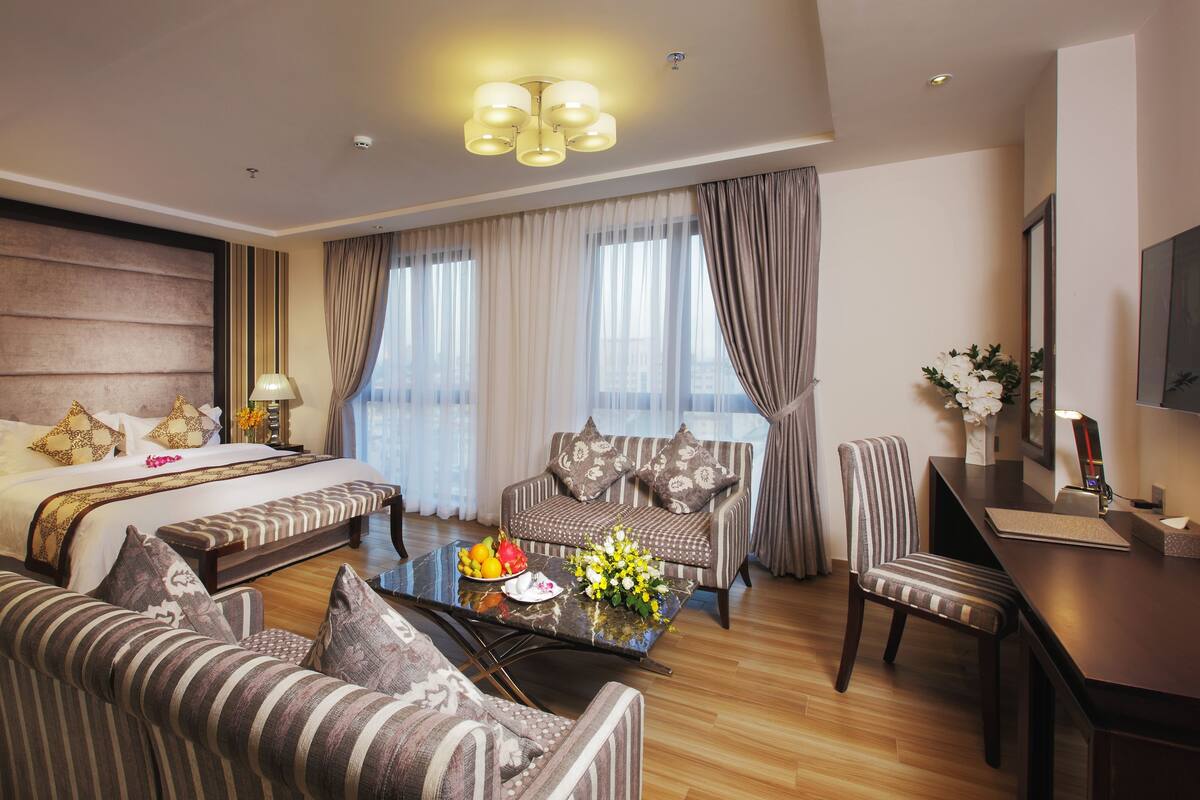 Habitación de hotel con una cama grande, un sofá, una mesa de comedor y un televisor.