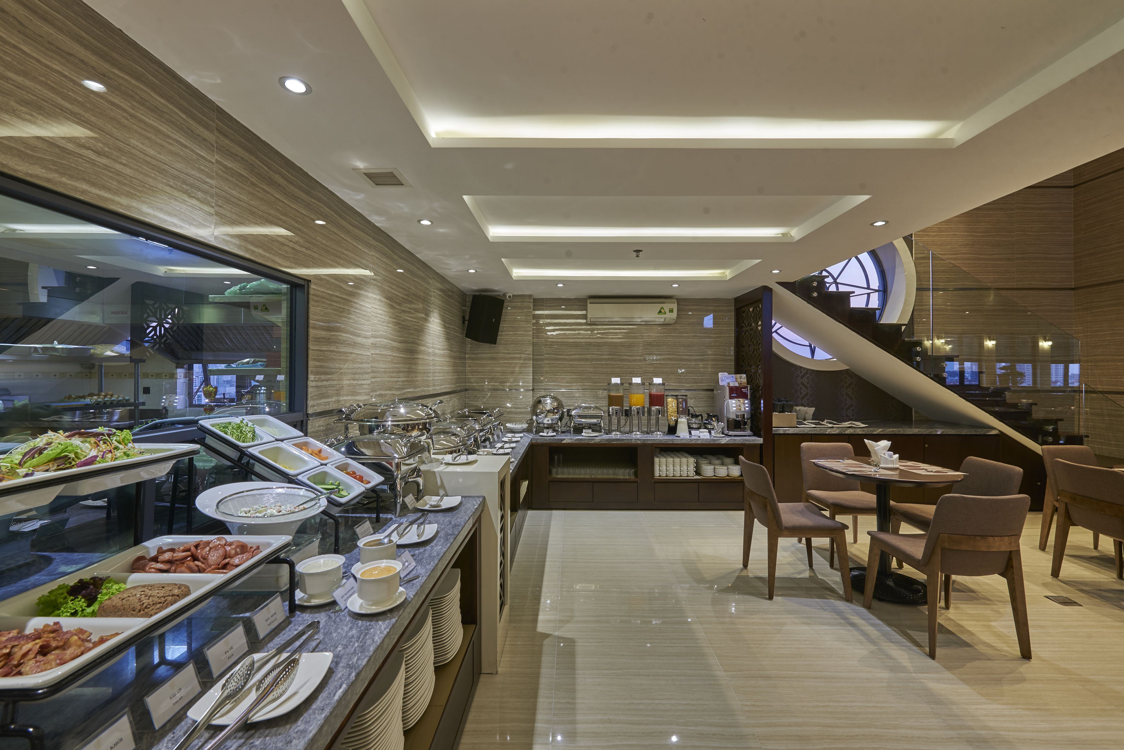 A modern buffet with various food stations, a seating area with tables and chairs, and a staircase leading to an upper level.