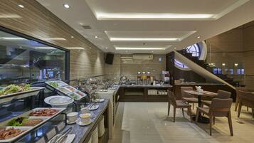 A modern buffet with various food stations, a seating area with tables and chairs, and a staircase leading to an upper level.