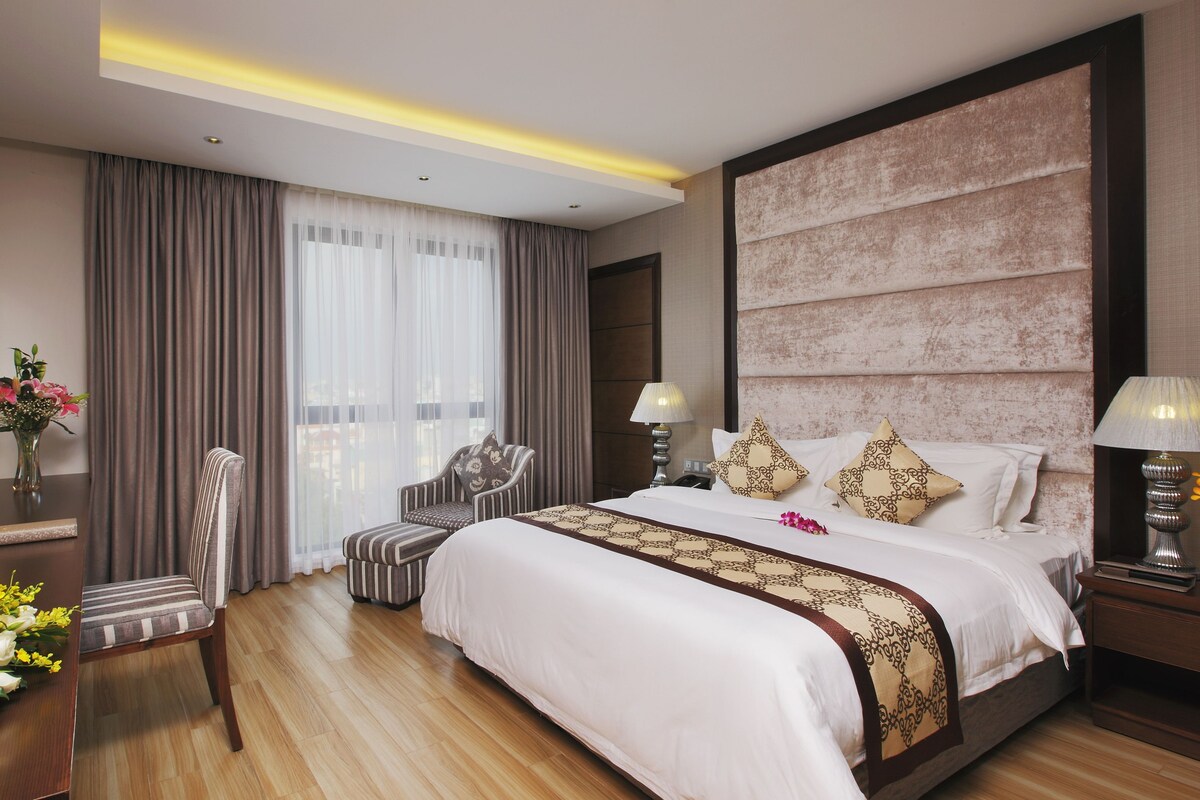Une chambre d’hôtel avec un grand lit, un bureau, une chaise, une table de chevet et une lampe.