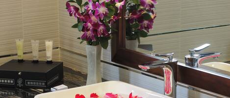 Ein Badezimmer mit einem rechteckigen Waschbecken, einem Spiegel, einer Vase mit Blumen und Pflegeprodukten.