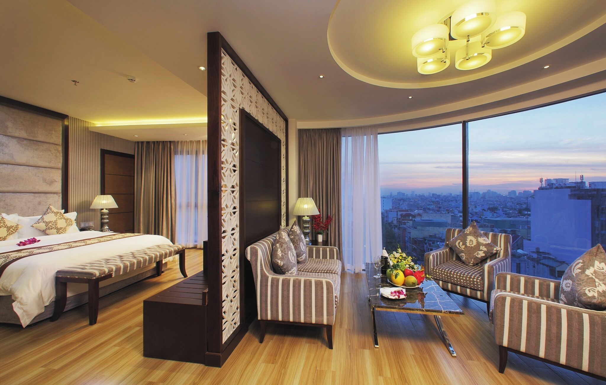 Ein Hotelzimmer mit einem großen Bett, zwei Sesseln, einem Couchtisch und Blick auf die Stadt.