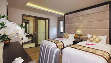 A hotel room with two beds, a nightstand, a lamp, a vase with flowers, and a view of a bathroom.