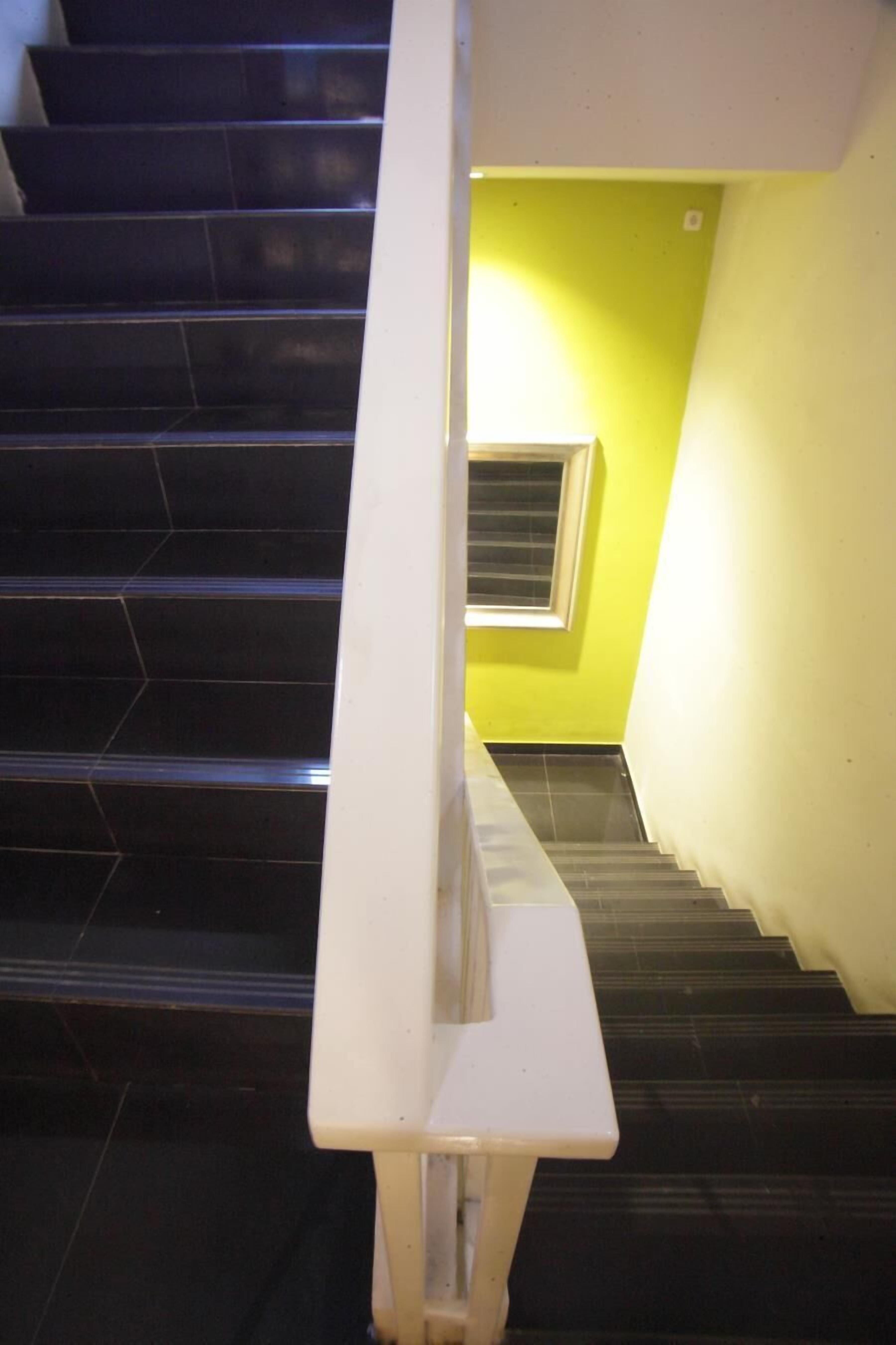 A staircase with black steps and a white handrail, leading to a room with a yellow wall and a window.