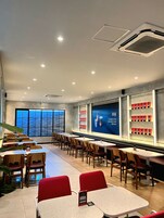 A modern restaurant with a view of the sea, featuring tables and chairs, a large display of signature Indonesian beans, and a ceiling with recessed lighting.