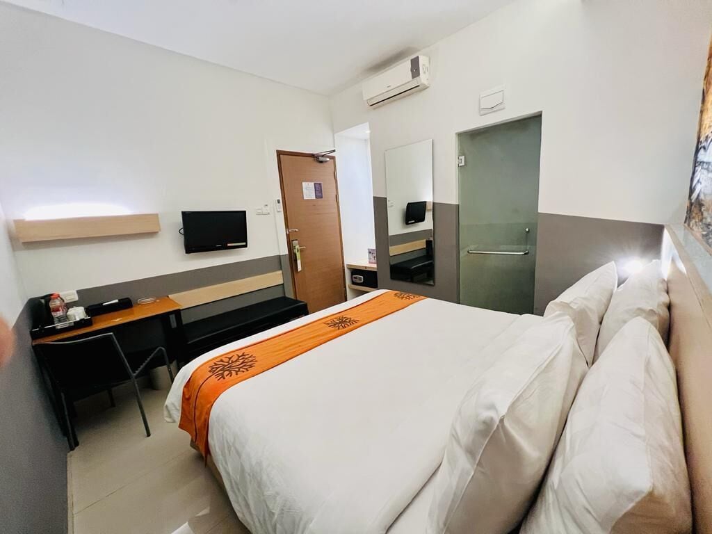 A hotel room with a bed, a desk, a chair, a television, a mirror, and a door.