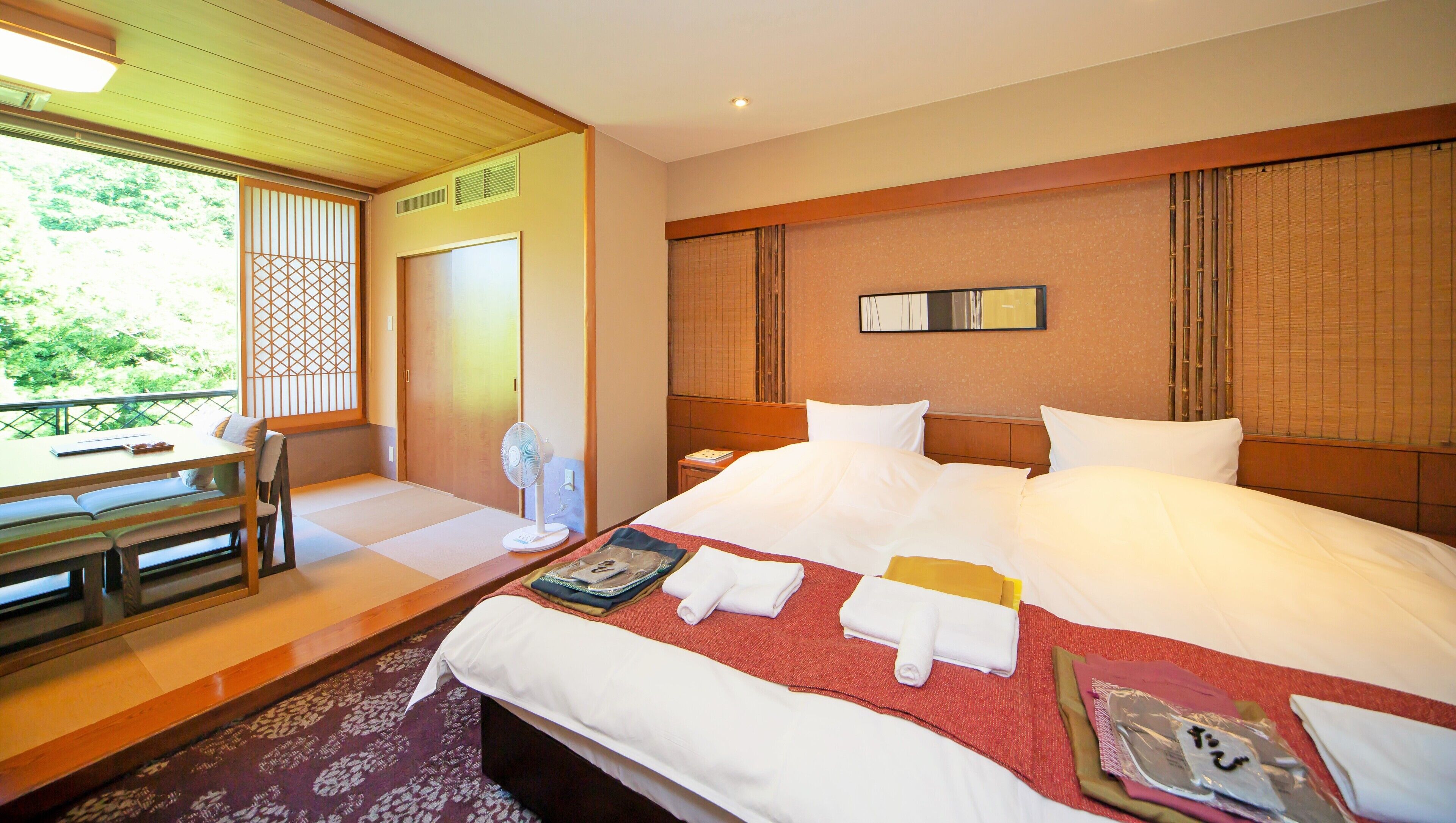 A hotel room with a bed, bedside table, chair, and a view of greenery outside.