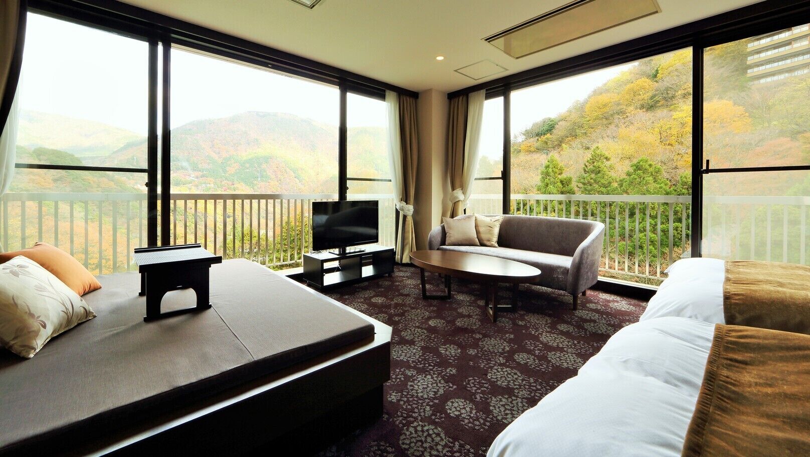A hotel room with a bed, sofa, TV, and a balcony with a view of hills.