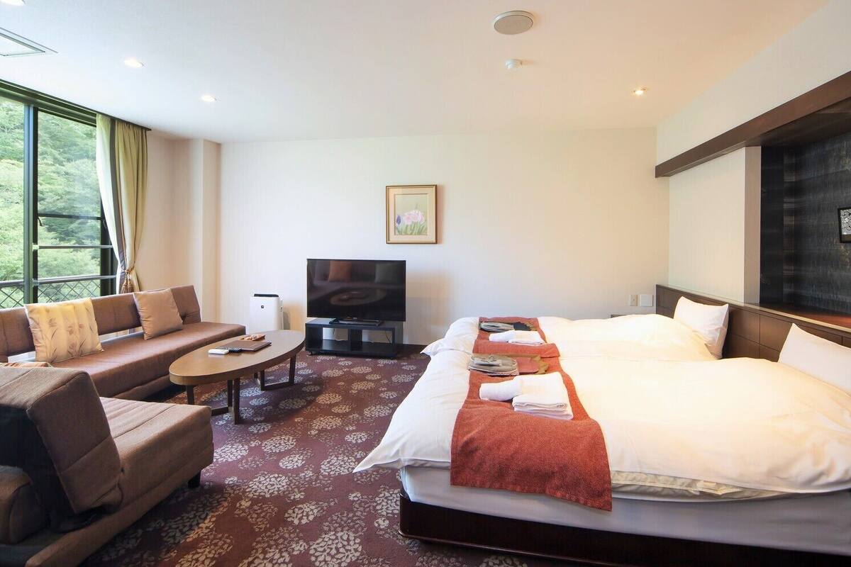 Une chambre d’hôtel avec un lit, un canapé, une télévision et une vue sur la verdure.