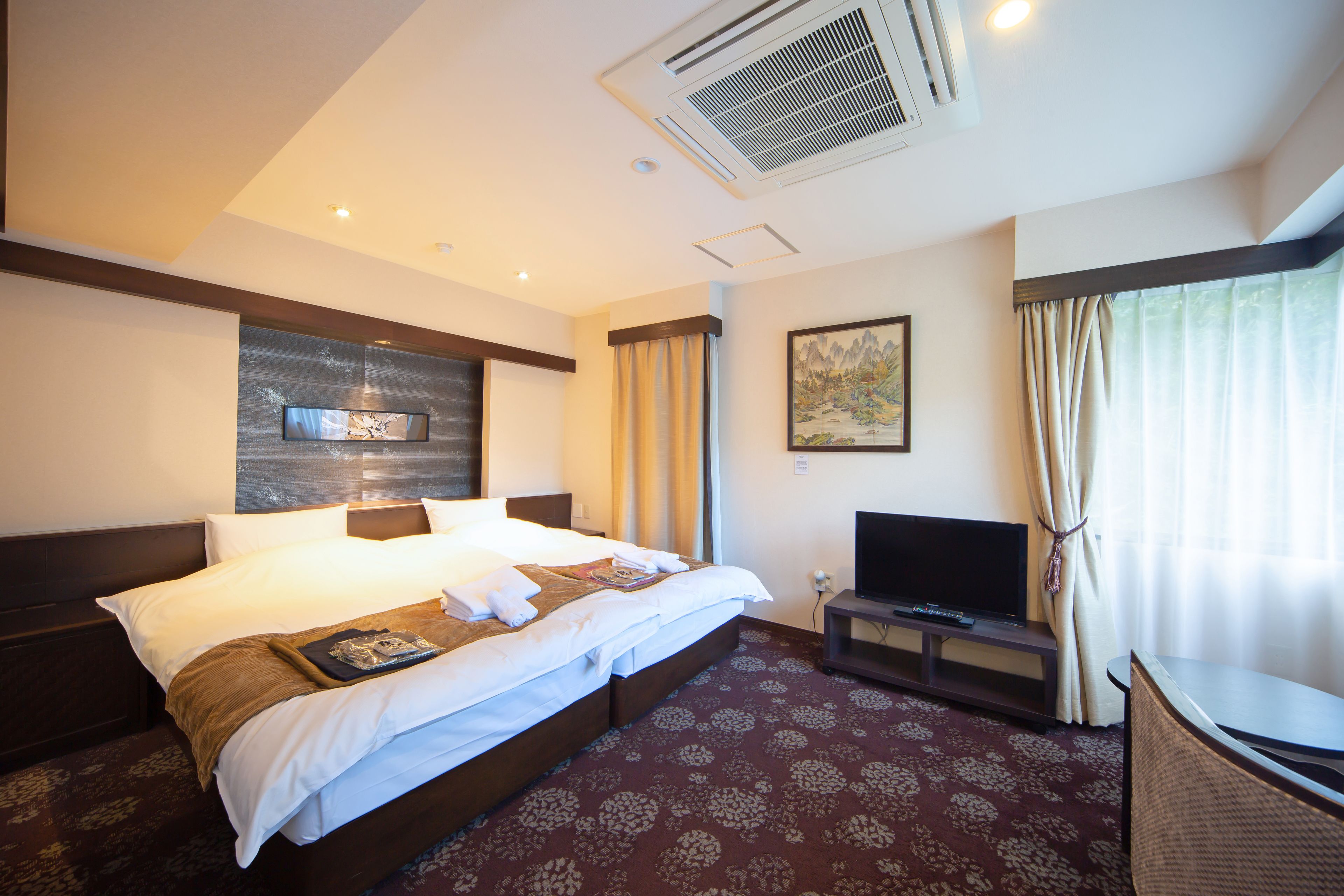 A hotel room with a large bed, a flat-screen TV, a desk, and a window with curtains.