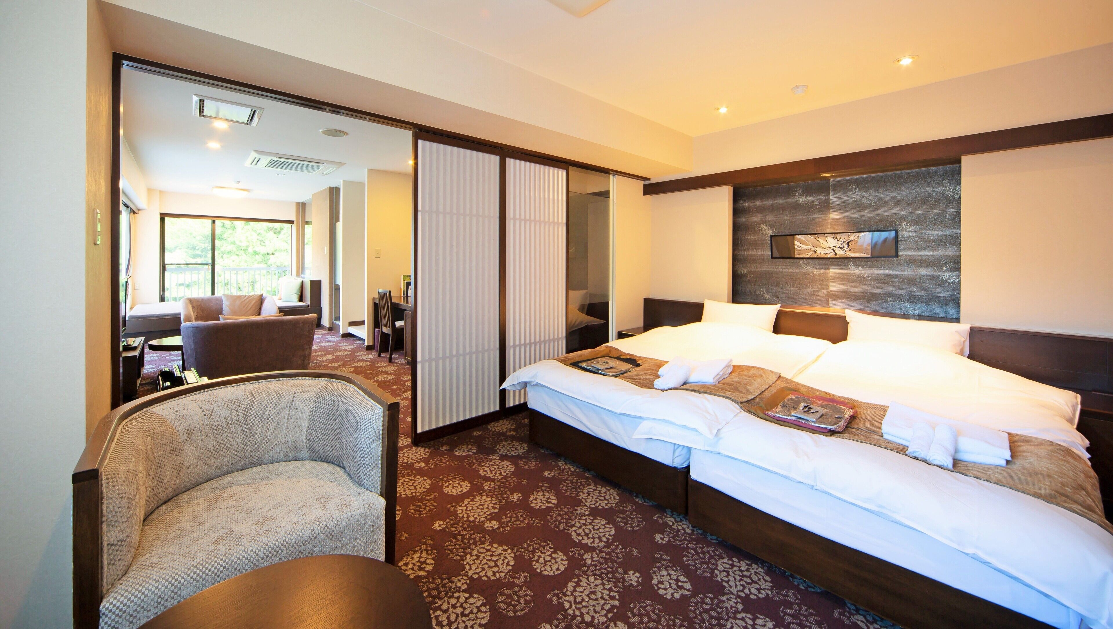 Een hotelkamer met een groot bed, een zithoek met een stoel en een tafel, en uitzicht door een schuifdeur.