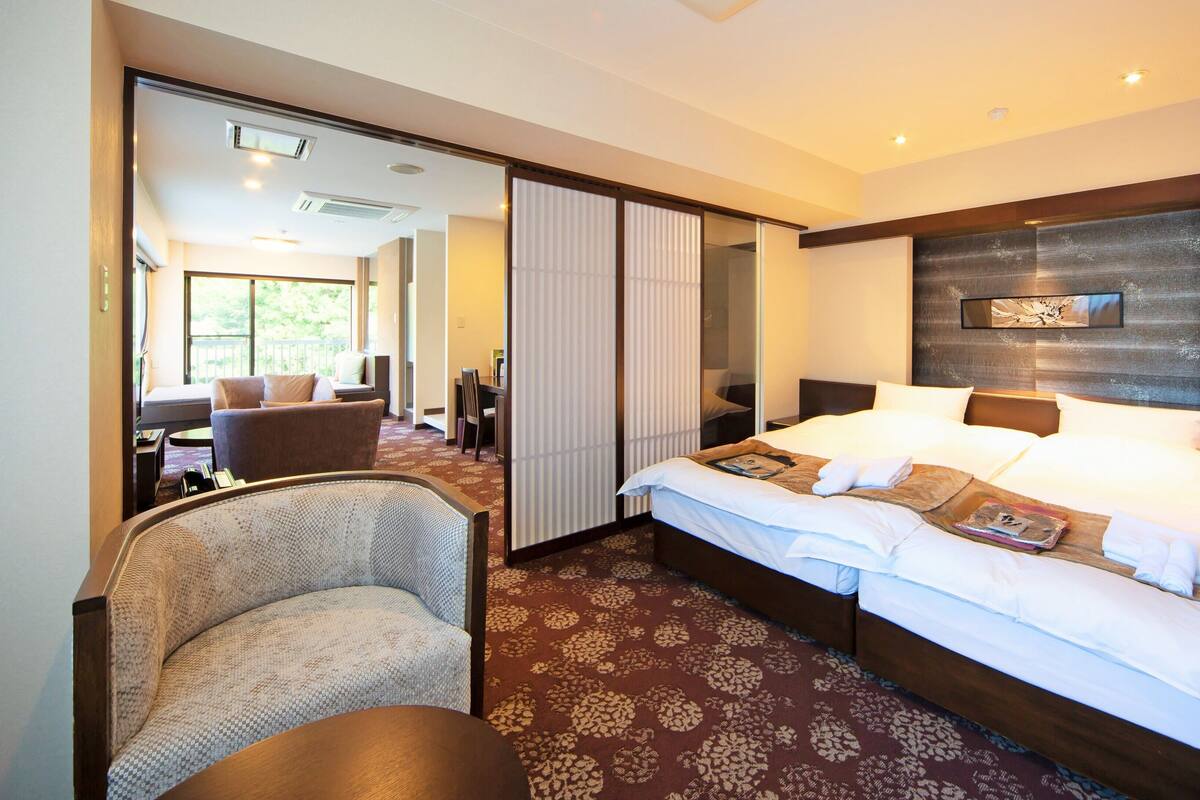 Une chambre d’hôtel avec un grand lit, un coin salon comprenant une chaise et une table, et une vue accessible par une porte coulissante.