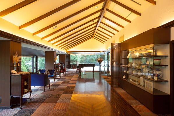 Een ruime lobby met een hoge plafond, een piano en een presentatie van decoratieve objecten.