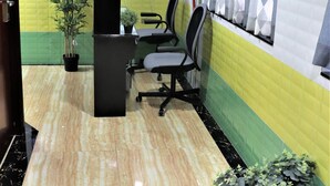 A reception area with a black desk, two office chairs, a potted plant, and a decorative wall with geometric patterns. - Sydney Hostel (Kowloon)
