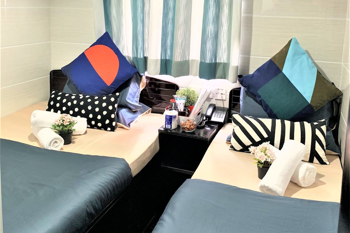 Habitación de hotel con dos camas, una mesita con artículos de aseo, un teléfono y una ventana con cortinas.