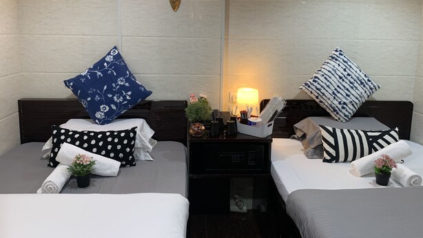 A hotel room with two beds, each with a pillow, a bedside table with a lamp, and a small plant. - Sydney Hostel (Kowloon)