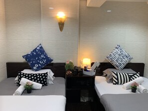 A hotel room with two beds, each with a pillow, a bedside table with a lamp, and a small plant. - Sydney Hostel (Kowloon)