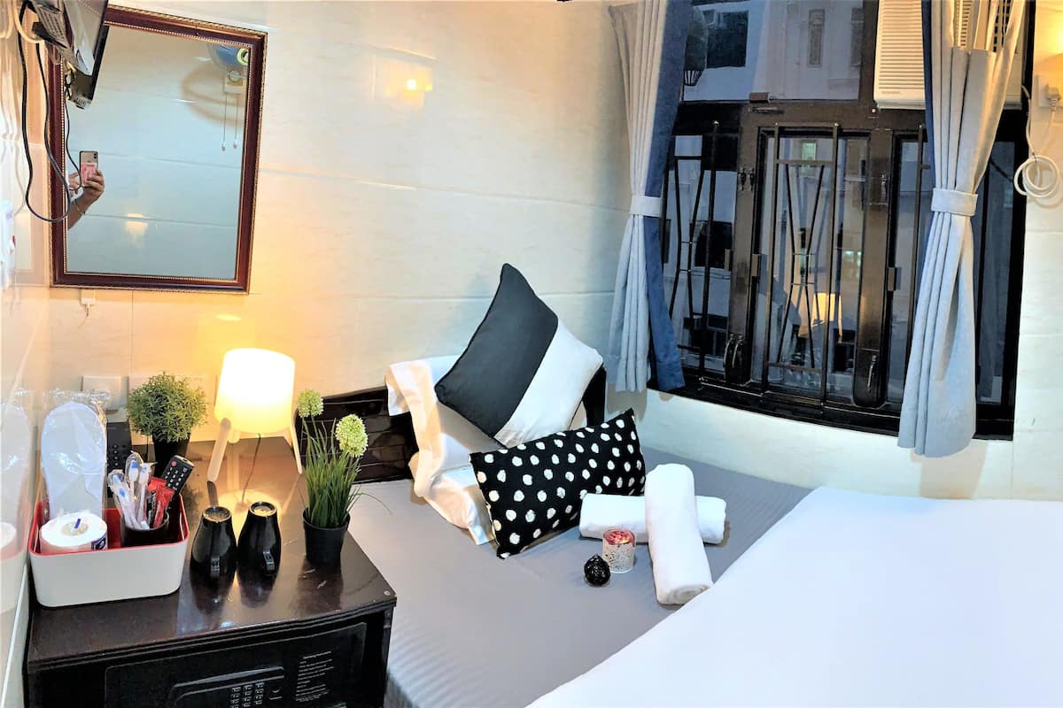 Una habitación de hotel con cama, mesita de noche, lámpara y ventana con cortinas.