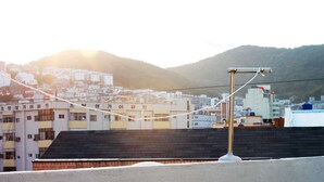 A rooftop with a metal structure, possibly for a telescope or antenna, overlooking a cityscape with buildings and a hill in the background. - Welcome Busan Guesthouse (Busan)