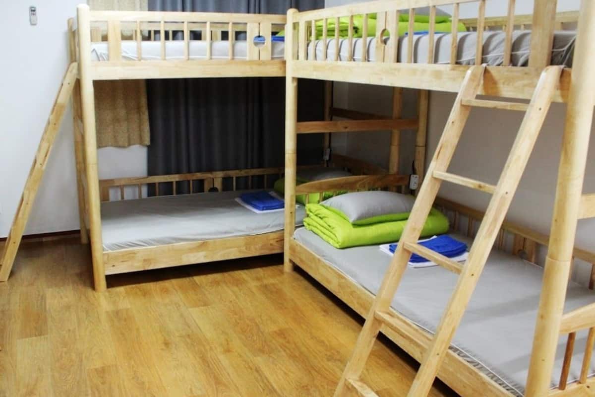 A bunk bed room with two beds, wooden flooring, and a window with curtains.