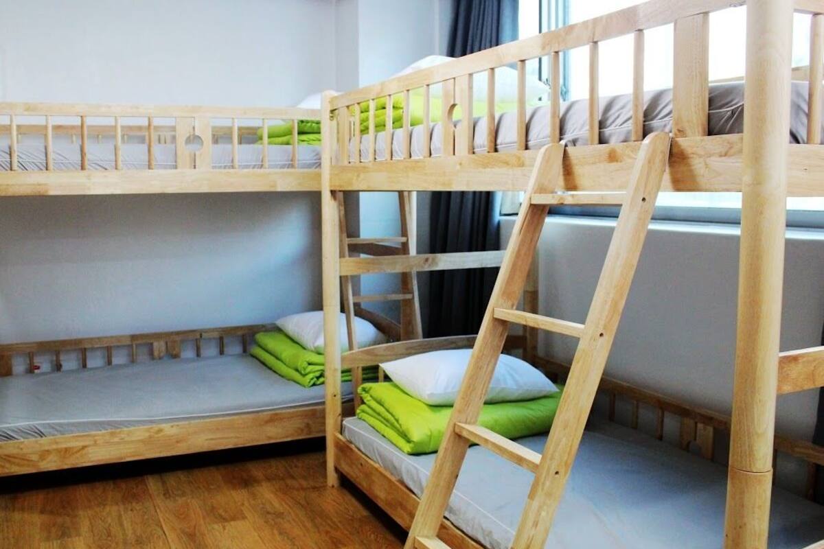 A bunk bed room with wooden frames, green and white bedding, and a ladder.