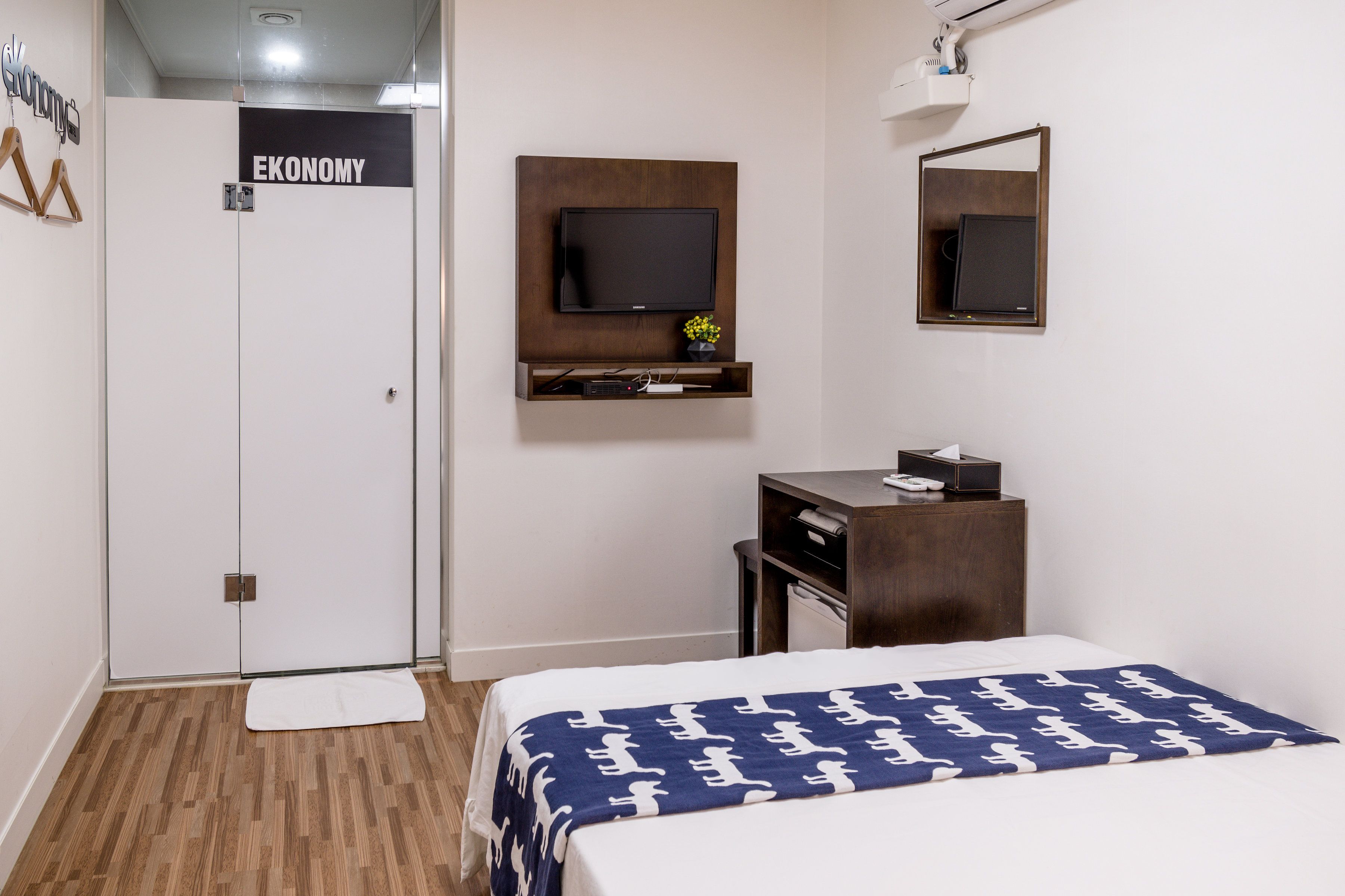 A hotel room with a bed, a desk, a TV mounted on the wall, and a wardrobe.