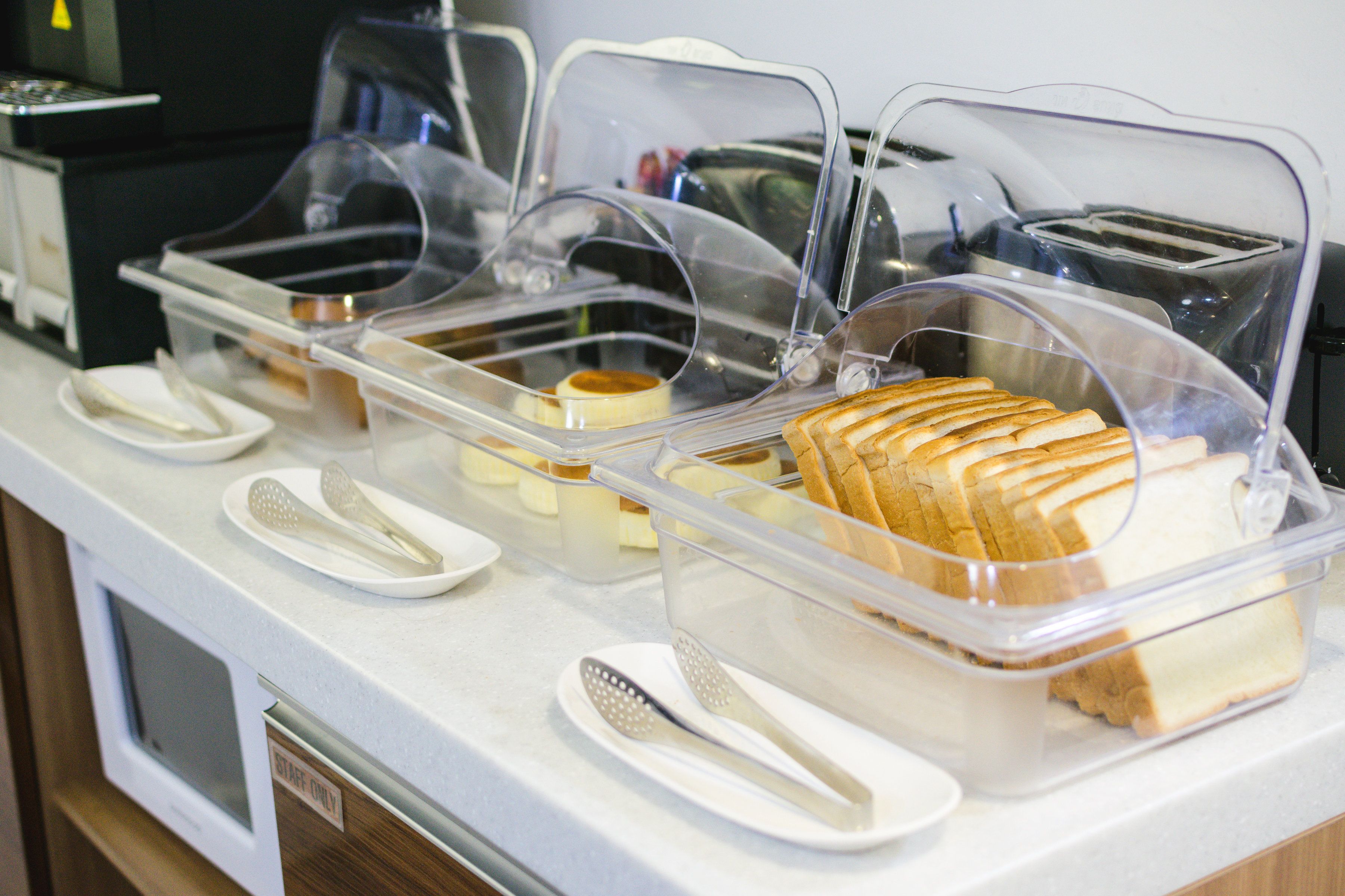 Un buffet de petit-déjeuner avec des récipients en plastique transparent contenant du pain, du beurre et diverses garnitures.