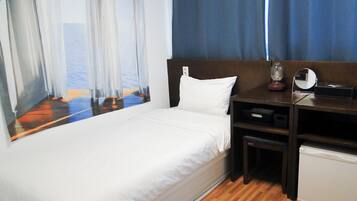 A hotel room with a bed, a desk with a mirror, and a view of the sea through sheer curtains.